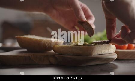 Man put steak slices on on small ciabatta bun for sandwich on kitchen countertop, wide photo Stock Photo