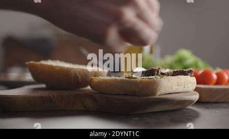 Man put steak slices on on small ciabatta bun for sandwich on kitchen countertop, wide photo Stock Photo