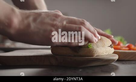 Man put top bun on steak ciabatta sandwich on kitchen countertop, wide photo Stock Photo