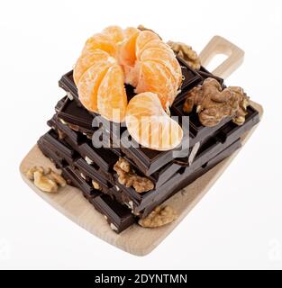 Peeled tangerine with walnuts on the pyramid of the pieces of the dark chocolate. Closeup image Stock Photo