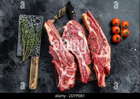 Assortment of raw cuts beef meat steaks on the bone. Black background. Top view Stock Photo