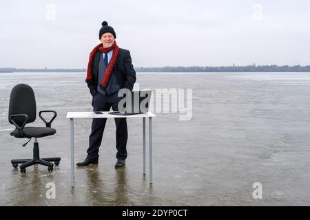 businessman in suit stands at a table and chair in the middle frozen lake Stock Photo