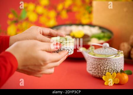 Hands of woman holding small cup of green tea she is drinking when celebrating Chinese New Year Stock Photo