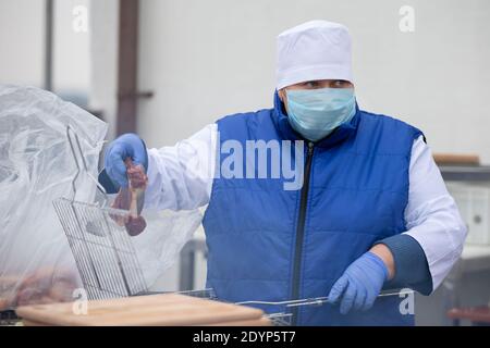 November 13, 2020. Belarus, Gomil region. PA Cooking street food during the coronavirus panademy. Chef in a medical mask with prepares meat. Stock Photo