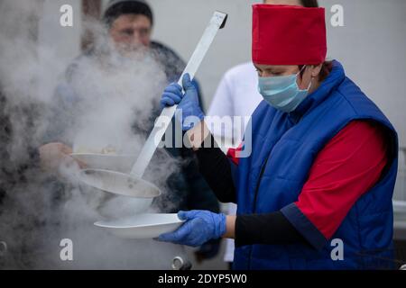 Cooking street food during the coronavirus panademy. A chef in a medical mask with a large scoop pours so Stock Photo
