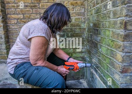 Woman drilling hole in outside wall of house. Stock Photo