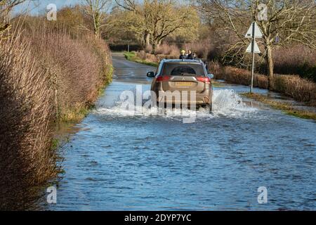 Wytham, Oxfordshire, UK. 27 December, 2020. Cars drive through the flooded road from Wytham to Wolvercote. Flooding in Oxfordshire. Storm Bella brought even more rain to Oxfordshire causing flooding in low lying areas. Plenty of people are out exercising in the sunshine. Credit: Sidney Bruere/Alamy Live News Stock Photo