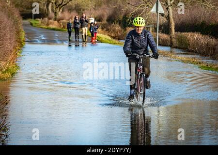 Wytham, Oxfordshire, UK. 27 December, 2020. A Cyclist rides across a flooded road from Wolvercote to Wytham. Flooding in Oxfordshire. Storm Bella brought even more rain to Oxfordshire causing flooding in low lying areas. Plenty of people are out exercising in the sunshine. Credit: Sidney Bruere/Alamy Live News Stock Photo