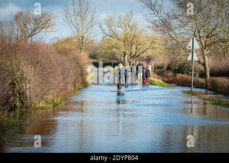 Wytham, Oxfordshire, UK. 27 December, 2020. Cyclist rides across the flooded road from Wolvercote to Wytham. Flooding in Oxfordshire. Storm Bella brought even more rain to Oxfordshire causing flooding in low lying areas. Plenty of people are out exercising in the sunshine. Credit: Sidney Bruere/Alamy Live News Stock Photo