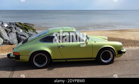 Classic Green Porsche motor car parked on seafront promenade sea in background. Stock Photo