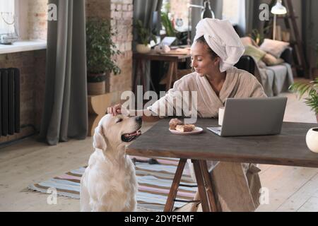 Happy woman loving her dog while having breakfast at the table in the morning Stock Photo