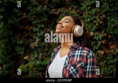 Cheerful woman in headphones rests in summer park Stock Photo