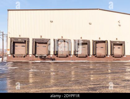 A warehouse with six loading docks with closed doors reflecting off of a wet parking lot on a sunny winter day in Braddock, Pennsylvania, USA Stock Photo