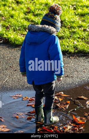 A small boy jumping in a puddle and splashing wearing wellies in autumn Stock Photo