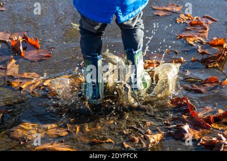 the legs of a child wearing wellies jumping in puddles splashing Stock Photo