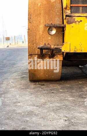Old rusty wheel of a yellow road roller on the newly constructed road close view Stock Photo