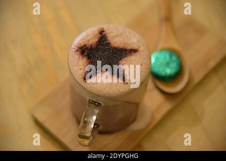 Christmas Hot Chocolate themed with a festive star, presented on a wooden server complete with a complimentary seasonal wrapped chocolate. Stock Photo