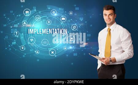Businessman thinking in front of technology related icons and IMPLEMENTATION inscription, modern technology concept Stock Photo