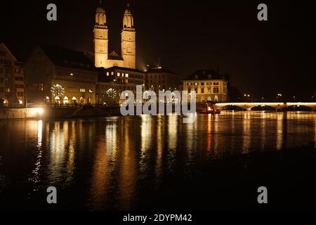 Major church Grossmünster in old town of zurich days before Christmas. View over bridge to a fire place on a raft on the river Limmat. Zurich, 19. Dec Stock Photo