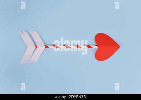 Simple paper cupid love arrow with heart shaped tip on blue background Stock Photo