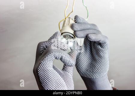 A guy in gray gloves is spinning a light bulb. Replacing the light bulb. Stock Photo