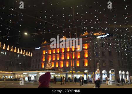 Red knitted hat in foreground at Paradeplatz at christmastime at night. Blurred illuminated windows of headquarter of banks and tram station in Zurich Stock Photo