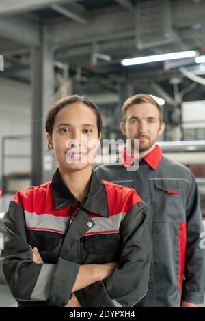 Young successful female leader of workteam keeping her arms crossed by chest while standing in front of camera against male colleague Stock Photo