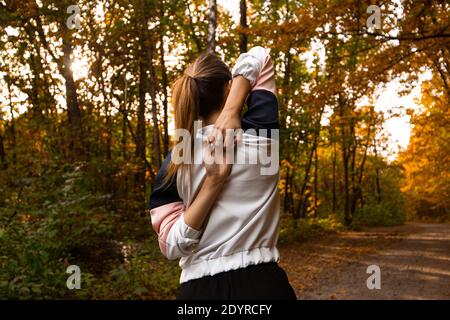 Woman doing exercise of hand to lock behind her back. Attractive young woman walking in park or forest. View from the back. Fit woman warm up and Stock Photo