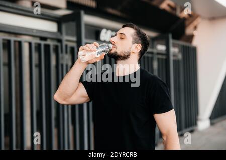 Man drinking water from plastic bottle after jogging with closed eyes. Hard workout. Take care of youself concept. Drink more water. Sport in big city Stock Photo