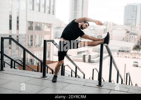 Strong man warming up. Morning activity. Man stretching his arms and looking away. Morning workout holding handrail. Black sportswear. Fit man doing Stock Photo
