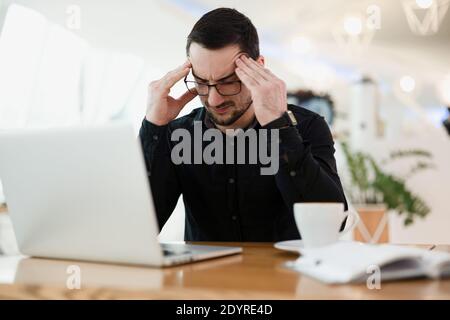 It doesn't work Tired male programmer massaging temples, holding head and looking for an error in the code. Remote or freelancer worker drinking Stock Photo