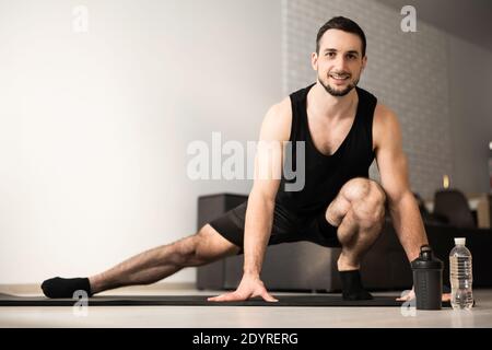 Sporty man doing side lunge exercise. Male athlete with fit body warming up, doing leg stretch workout at home. Take care of yourself Modern light Stock Photo