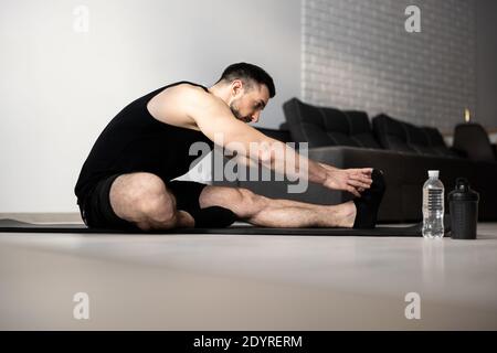 Stretch body exercise. Yoga position. Man stretching before workout. Black sportswear. Athletic man warming up on black yoga mat. Sports during Stock Photo