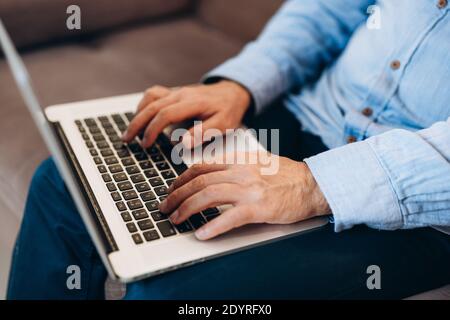 Close up male hands typing at keyboard. Middle aged man using modern laptop to read news or reply to emails. Blue shirt and jeans. Modern technology Stock Photo