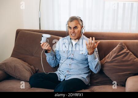Game over. Middle aged man playing game using console controlling joystick. Entertainment during the lockdown. Lost game. Living room on background Stock Photo