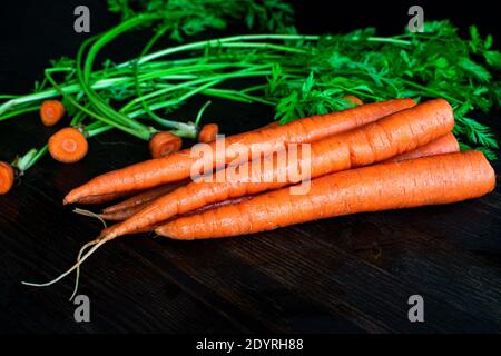 Organic Carrots on a Cutting Board: Removing the tops from carrots on a dark wood cutting board Stock Photo