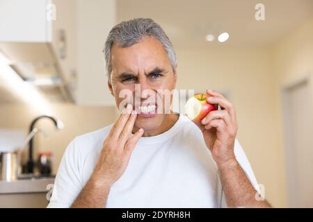 Toothache concept. Adult man broke a tooth when he bit an apple. Visit your dentist regularly Man in white t-shirt suffering from toothache, tooth Stock Photo