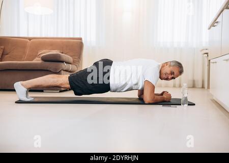 Plank it Confident senior man doing plank position while exercising on the floor in light loft interior. Hard workout. Training at home. Man training Stock Photo