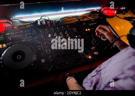 DJ plays live set and mixing music on turntable console at stage in the night club. Disc Jokey Hands on a sound mixer station at club party. DJ mixer Stock Photo