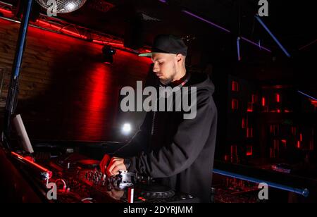 Confident DJ mixes music in cool night club. High tech concept. Bright red stage lights and silver disco ball at background. Fun, youth and Stock Photo