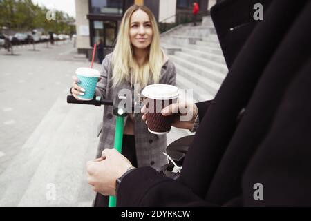 Coffee break Man and woman took a break from their electric scooter driving around town for a cup of delicious cappuccino. Attractive woman looking at Stock Photo