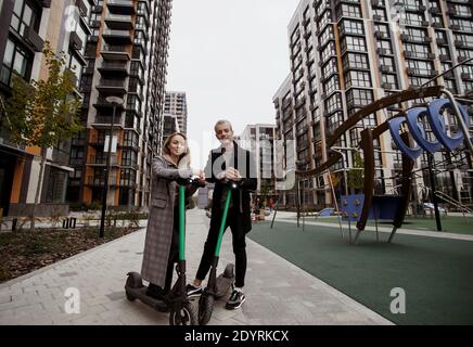 Young couple loves modern technology. Attractive blonde woman and good-looking man in smart casual clothes spend time together riding electrical Stock Photo