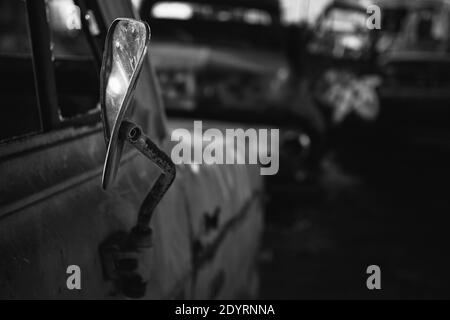 A grayscale shot of the broken mirror of an abandoned car with a blurry background Stock Photo