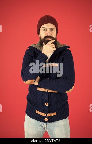 Warm and comfortable. Brutal temper. Fashion menswear shop. Masculine clothes concept. Winter menswear. Clothes design. Man bearded warm jumper and hat red background. Winter season menswear. Stock Photo