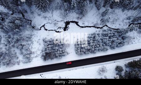 Aerial drone shot of a road with a car driving through the forest in winter Stock Photo