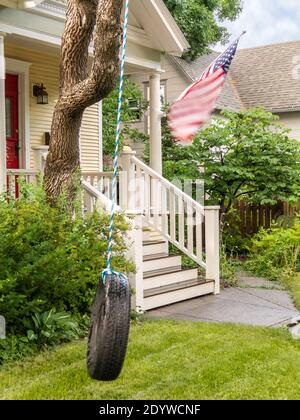 Wind from passing thunderstorm blows the American flag and the tire swing in the front yard of this colonial house - metaphor for threat to democracy Stock Photo