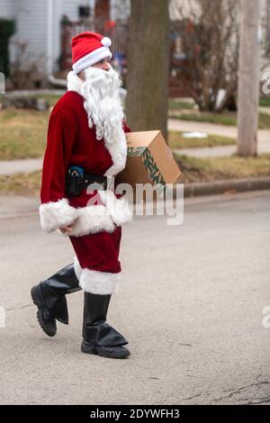 Winneconne, WI -23 December 2020: A USPS postal worker letter carrier is dressed up as Santa Claus as he delivers a package to a house. Stock Photo
