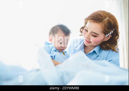 Asian mother and her son wearing blue shirts on bed in bedroom with copy space at home. People lifestyle and Newborn medical concept. State quarantine Stock Photo