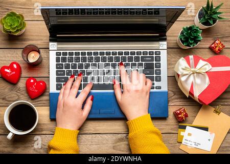 Girl hands, debit card, chooses gifts, makes purchase, tablet, coffee cup, two hearts, bag on wooden table Top view Flat lay Holiday shopping list Stock Photo