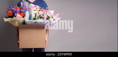 White male courier holding a large cardboard box with several bouquets, . High quality photo Stock Photo